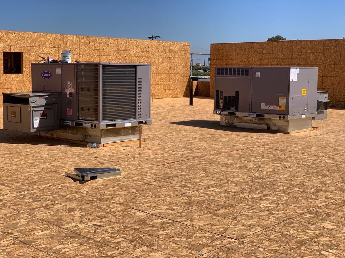 Two rooftop HVAC units on an unfinished wood surface. Blue sky visible.