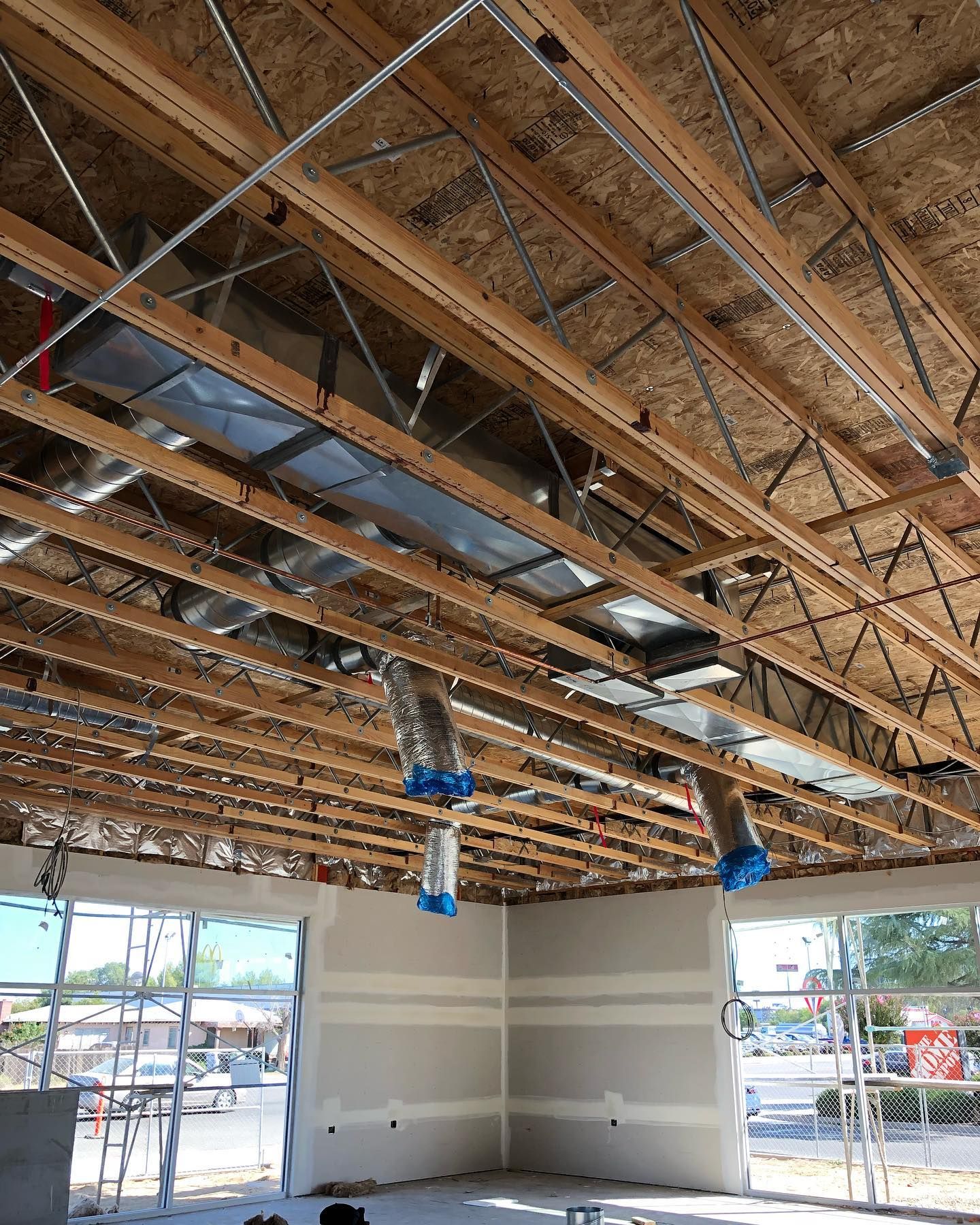 Construction site interior; exposed wooden beams, ductwork, and partially built walls, windows overlooking street.