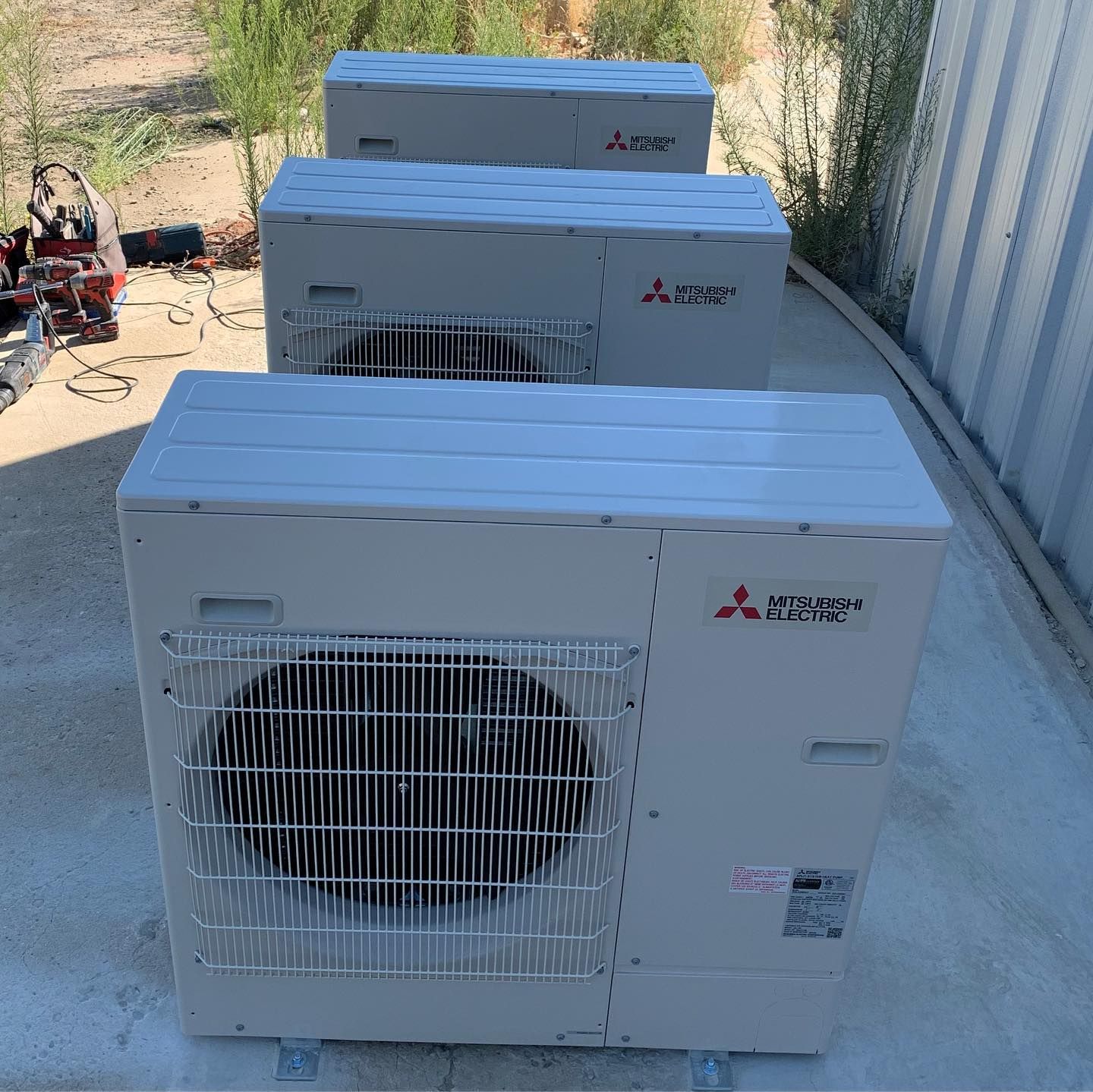 Three Mitsubishi air conditioning units outdoors on concrete.