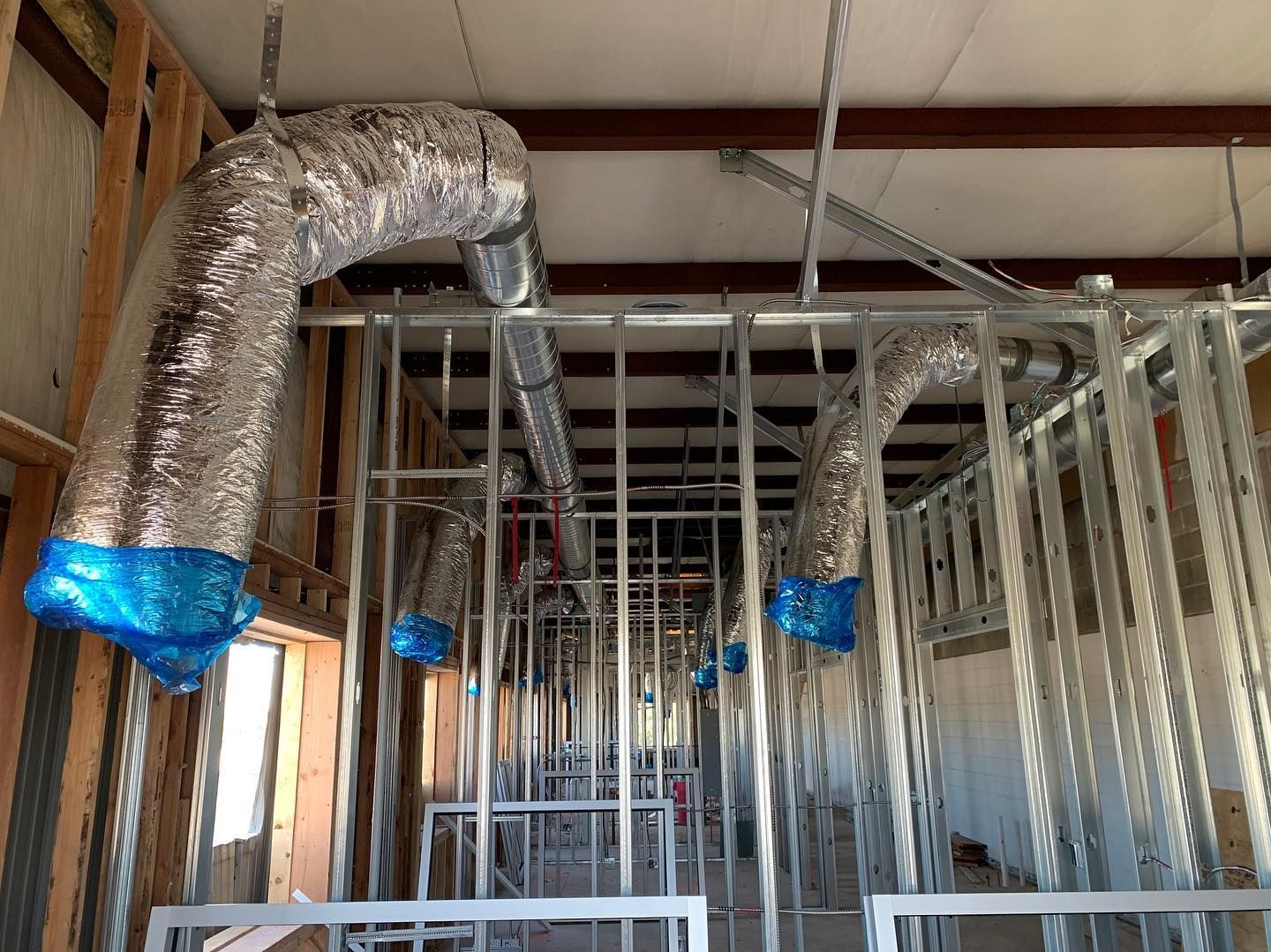Construction site interior with metal framing, HVAC ductwork, and unfinished walls.