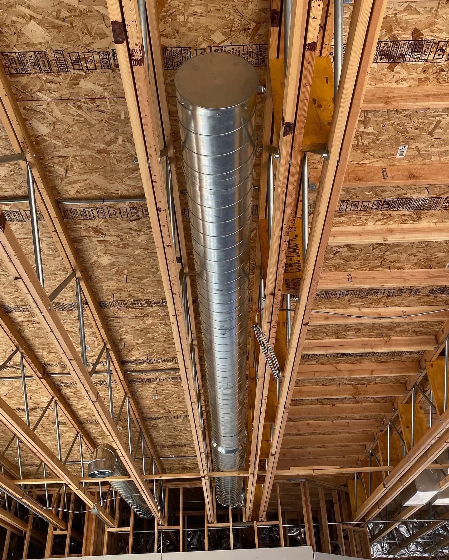 Construction of a ceiling with exposed wood beams and a long, cylindrical metal air duct.