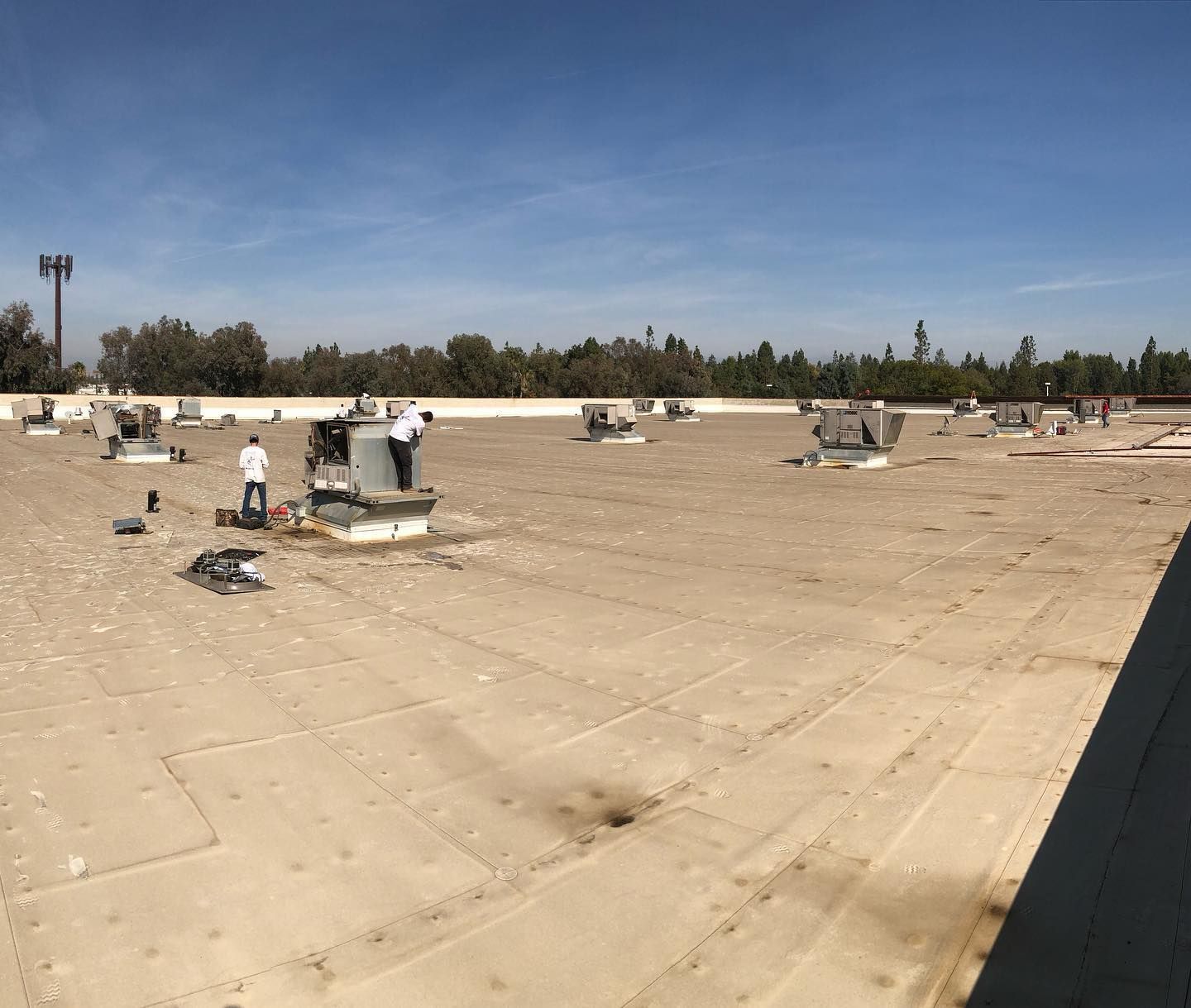 Workers on a flat commercial roof, installing or repairing HVAC units; sunny day.