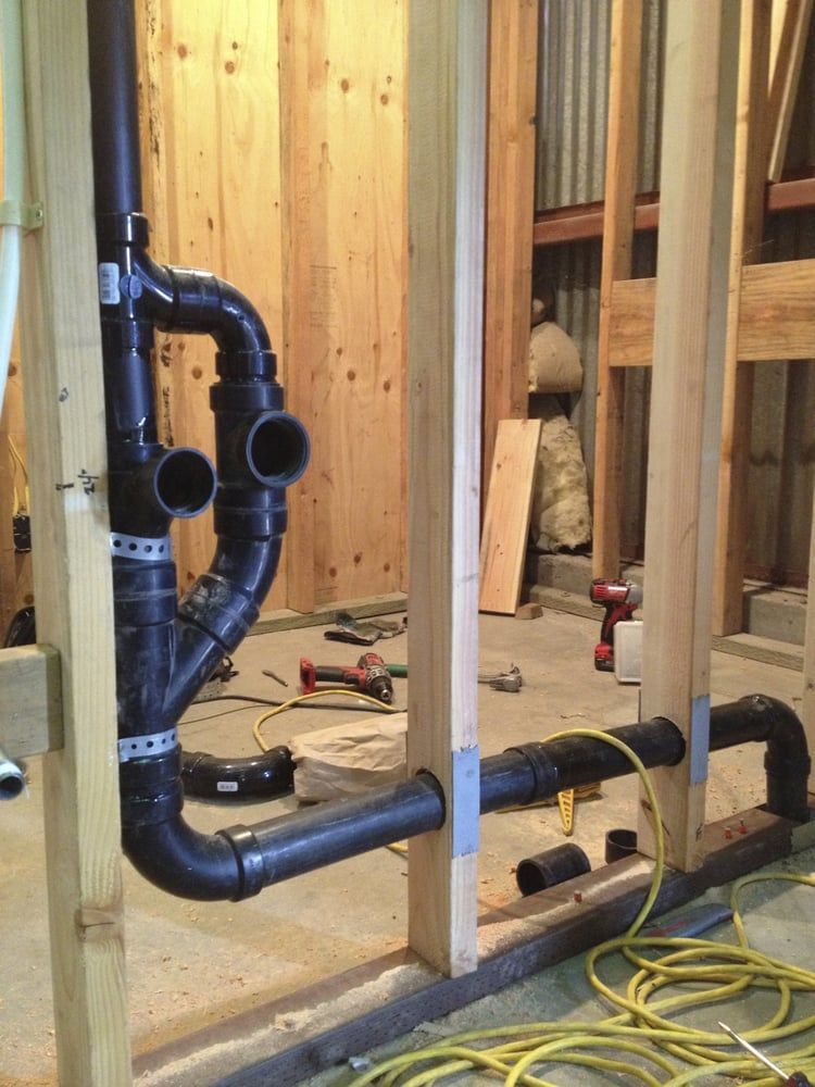 Black plumbing pipes being installed inside wooden framing in a construction setting.