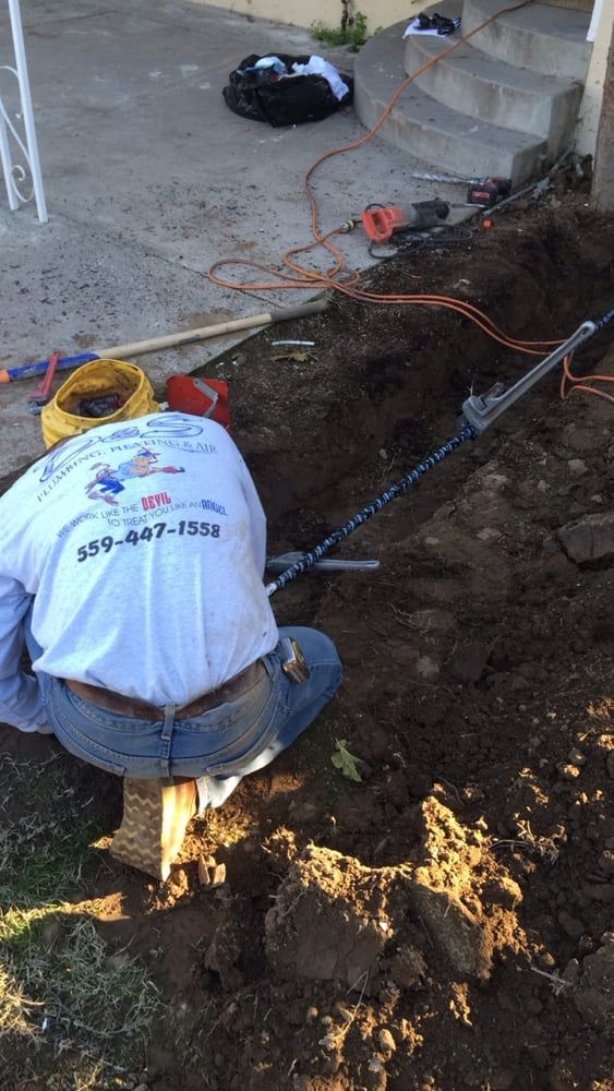 Man kneeling in a trench, working on a utility line near concrete steps.