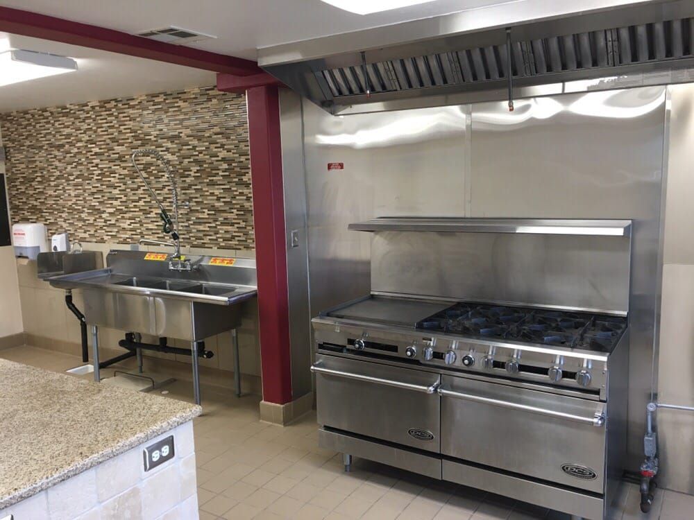 Commercial kitchen with stainless steel appliances, stove, sink, and stone backsplash.