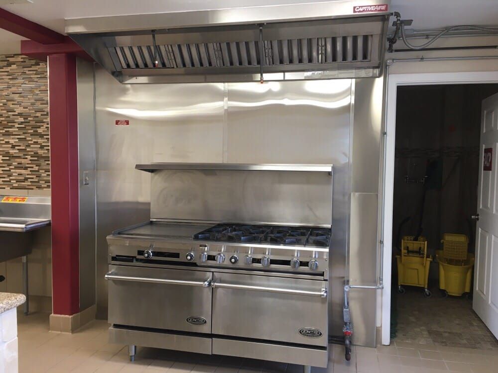 Stainless steel commercial kitchen range with hood and shelves.