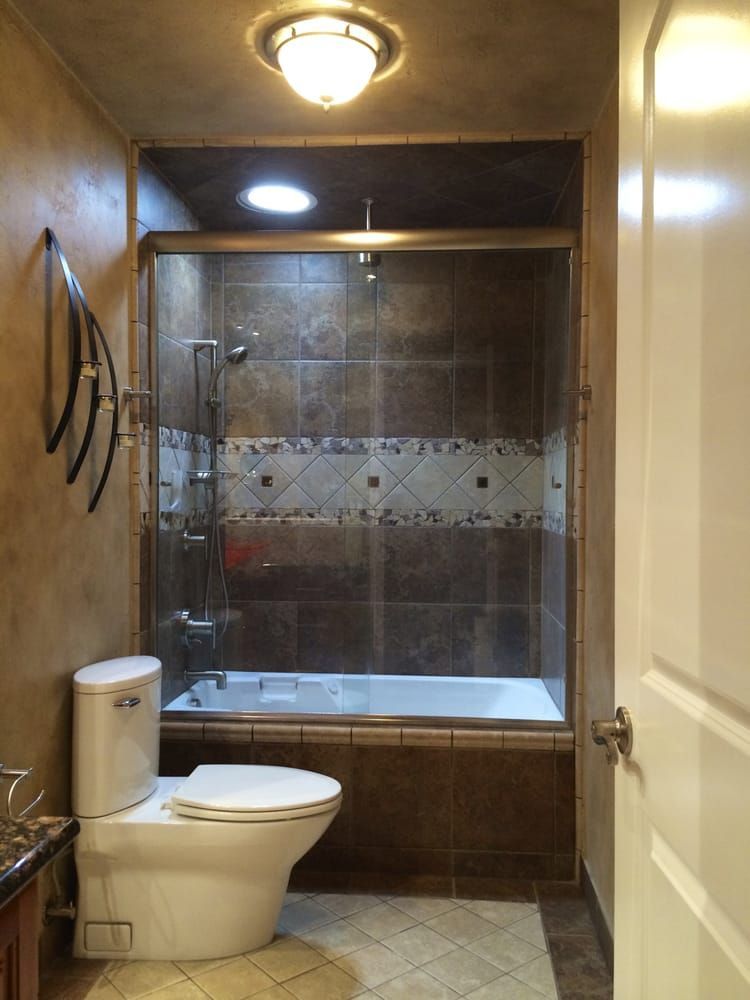 Bathroom with a toilet, bathtub/shower, and brown tiled walls.
