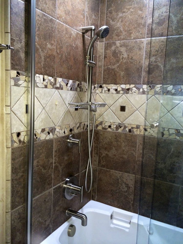 Brown tiled shower with a decorative accent strip, silver shower fixtures, and a glass door.