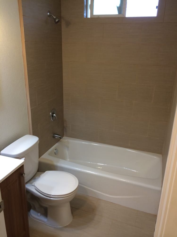 Bathroom with a toilet, tub, shower, and tan tile walls.