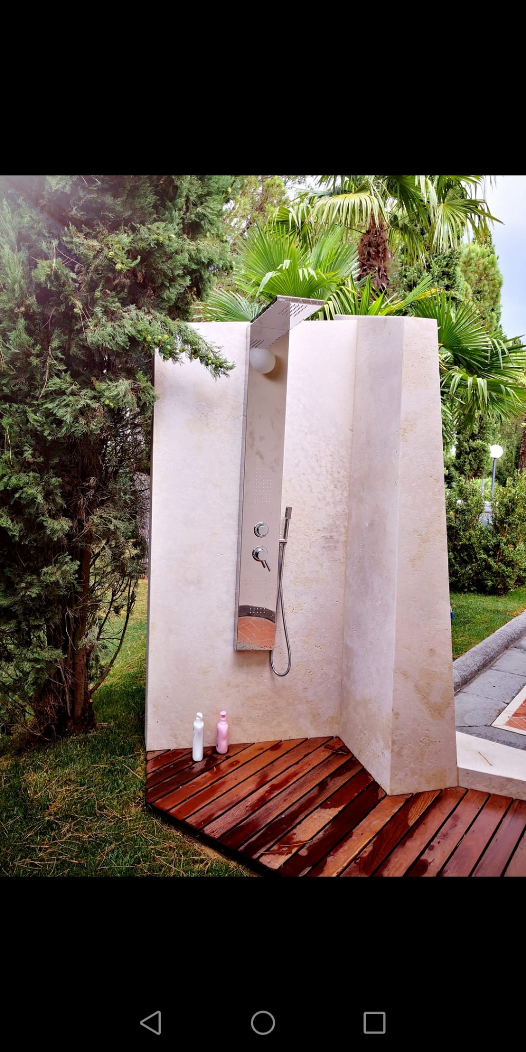 Una doccia esterna bianca con pavimento in legno e alberi sullo sfondo.