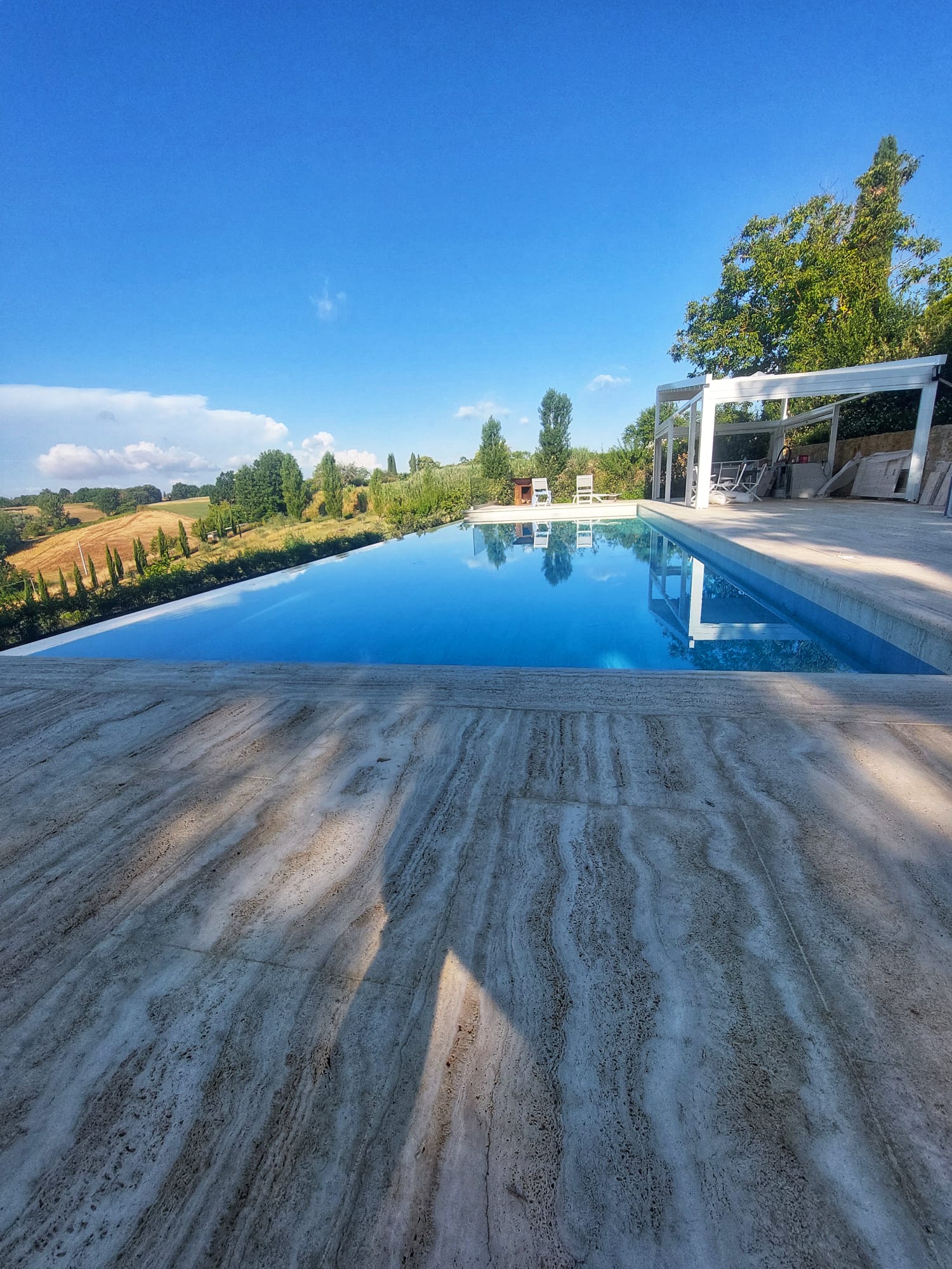 Una grande piscina circondata da alberi e un patio nelle giornate di sole.