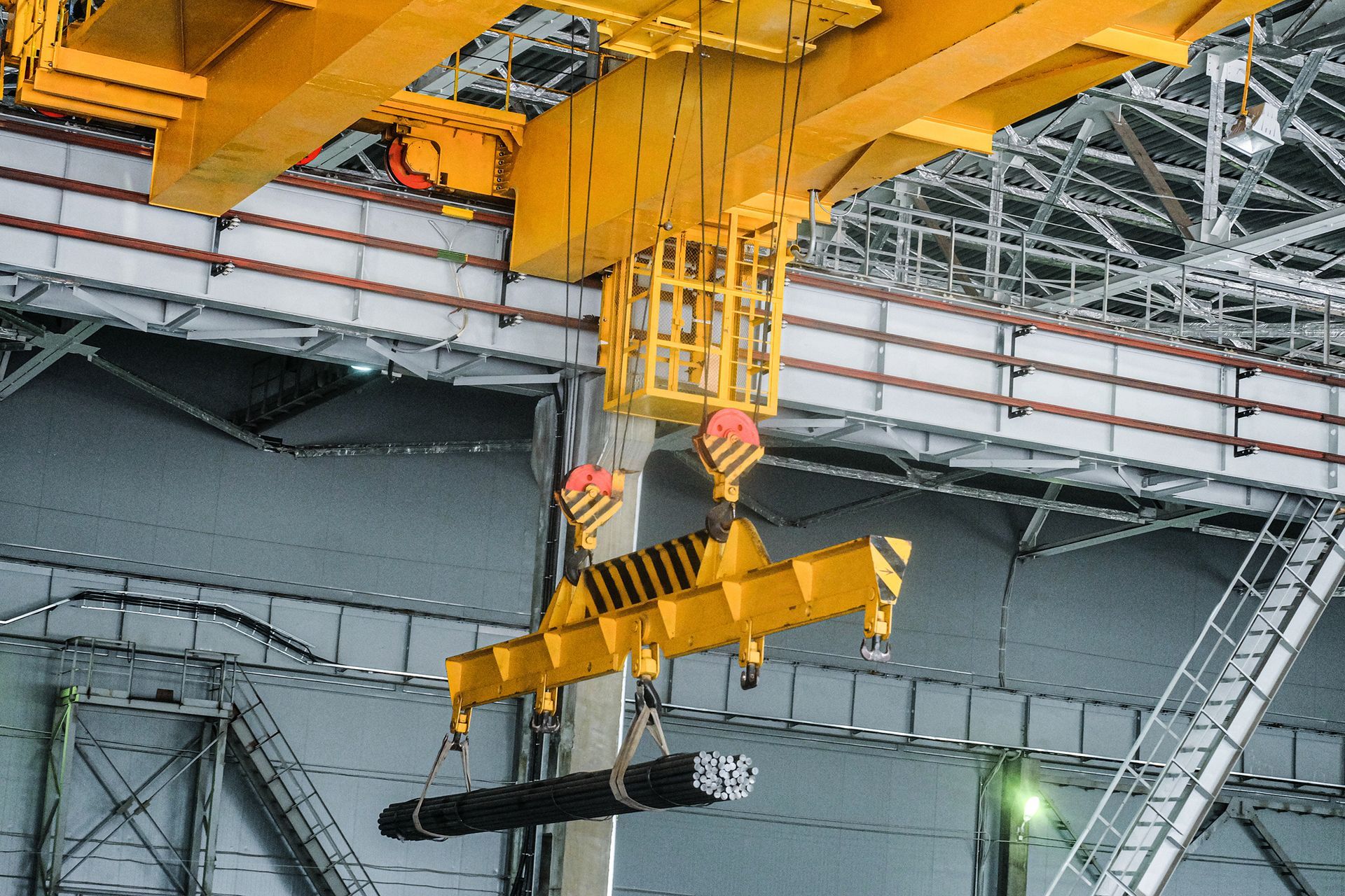 Overhead crane lifting bundled steel rods inside an industrial warehouse.