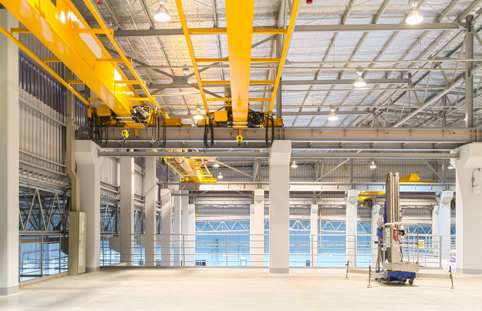 Empty industrial warehouse with bright yellow overhead cranes and a small lift platform