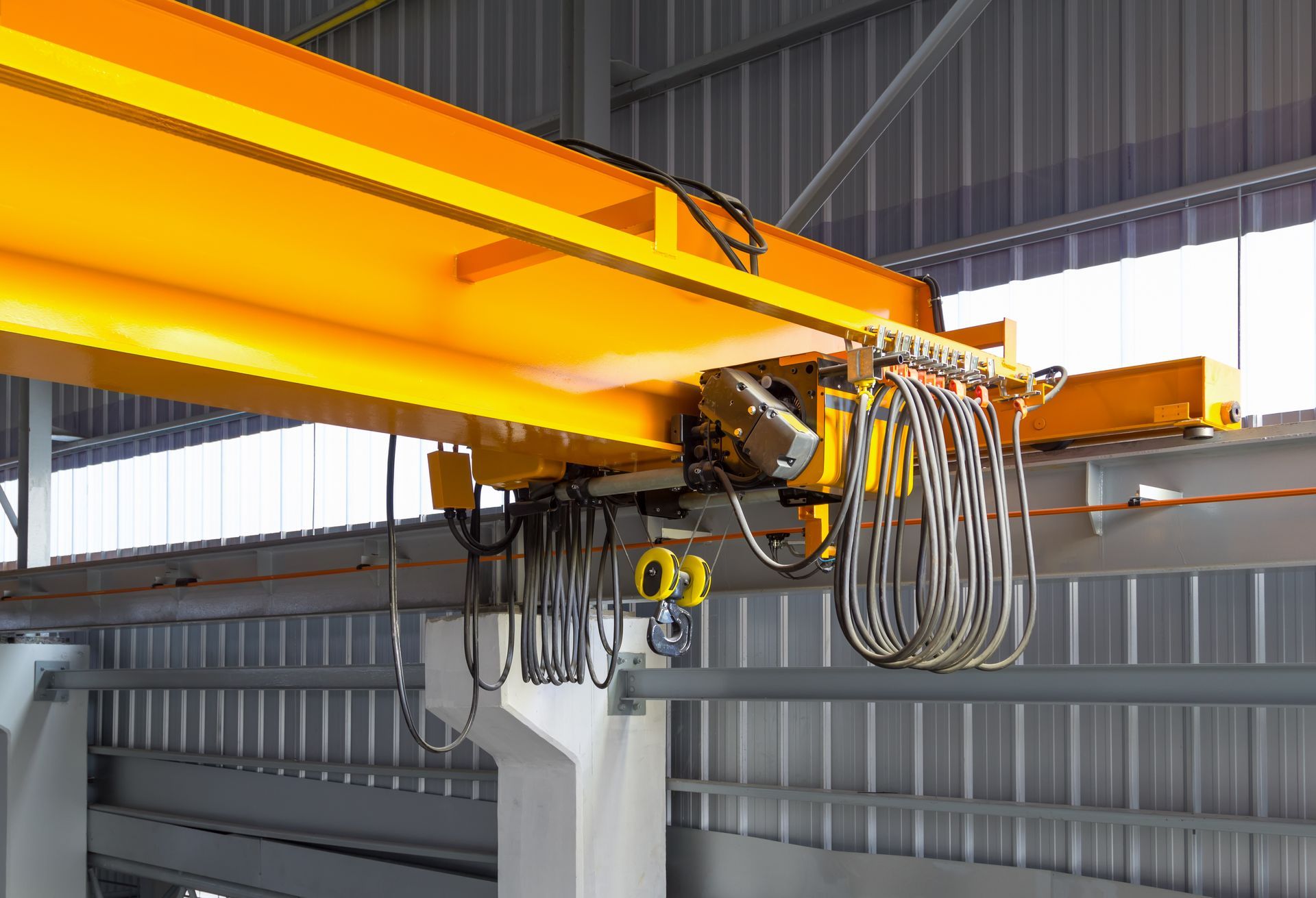 Yellow overhead crane rail system with suspended cables and hoist mechanism.