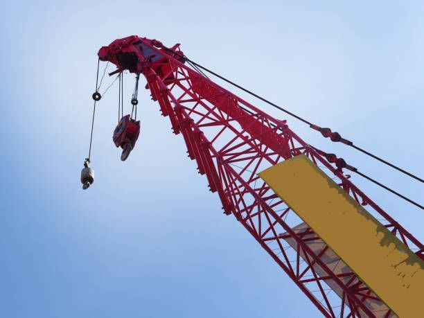 Image from below of a red and yellow crane, in front of the ble sky.