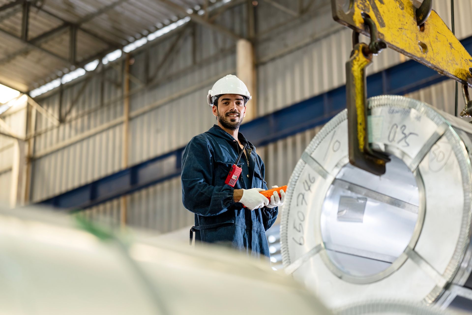Man in safety gear operates machinery in a factory, smiling, near a large metal coil.