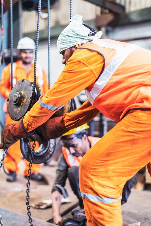 Close-up of a man in orange overalls performing crane repair service, alongside a couple of workers Close-up of a man in orange overalls performing crane repair service, alongside a couple of workers