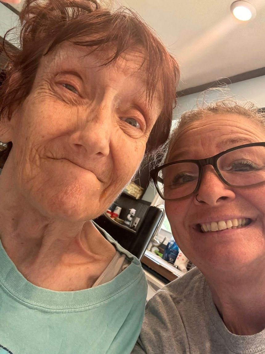 Two women smiling for a selfie; one older with light skin, one with glasses and fair skin.