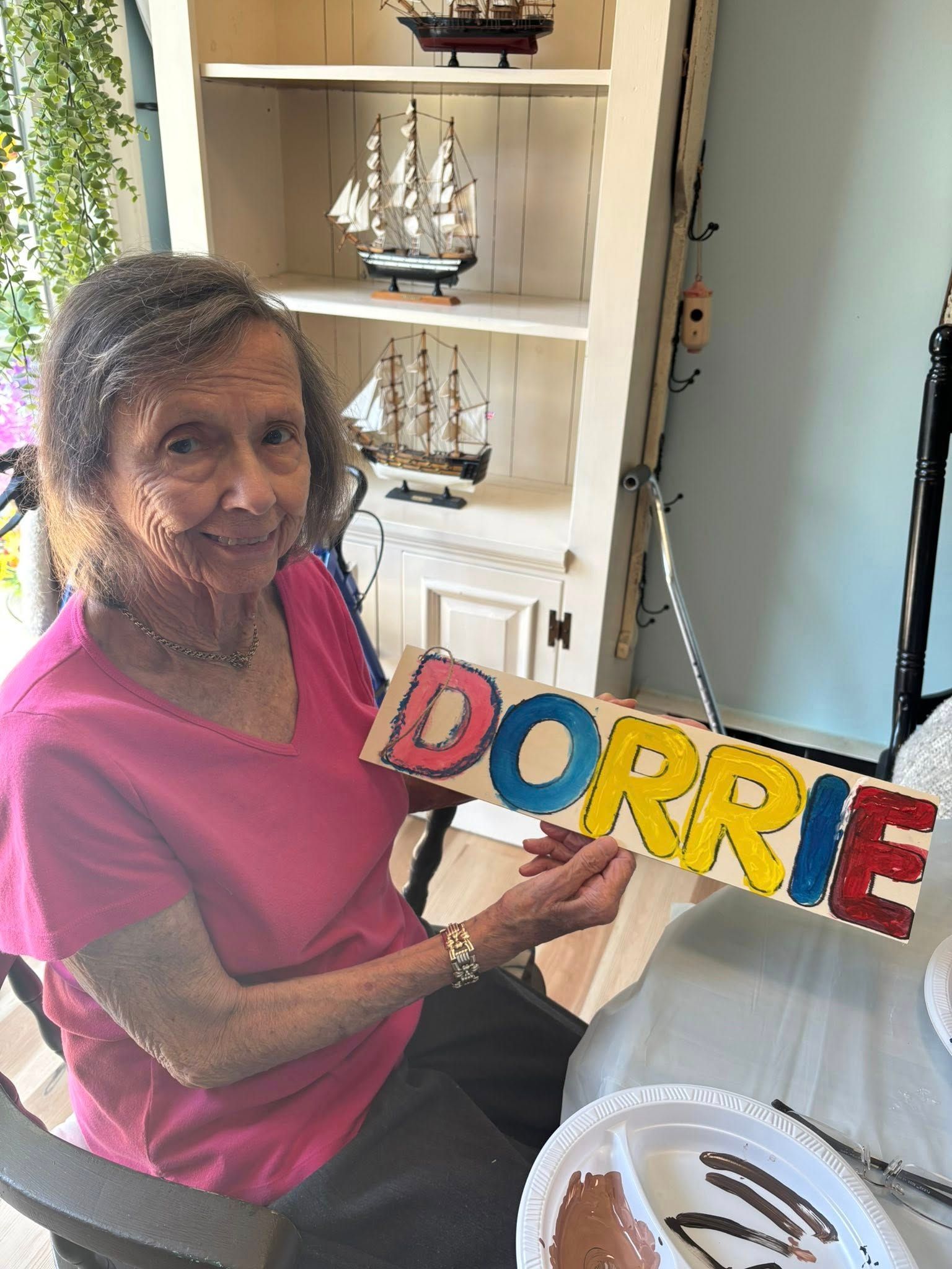 Elderly woman smiling, holding colorful painted sign 