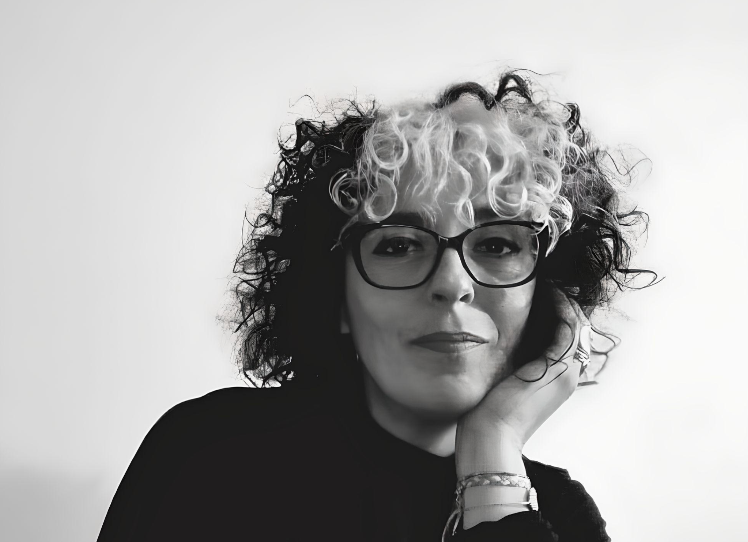a black and white photo of a woman with curly hair and glasses .