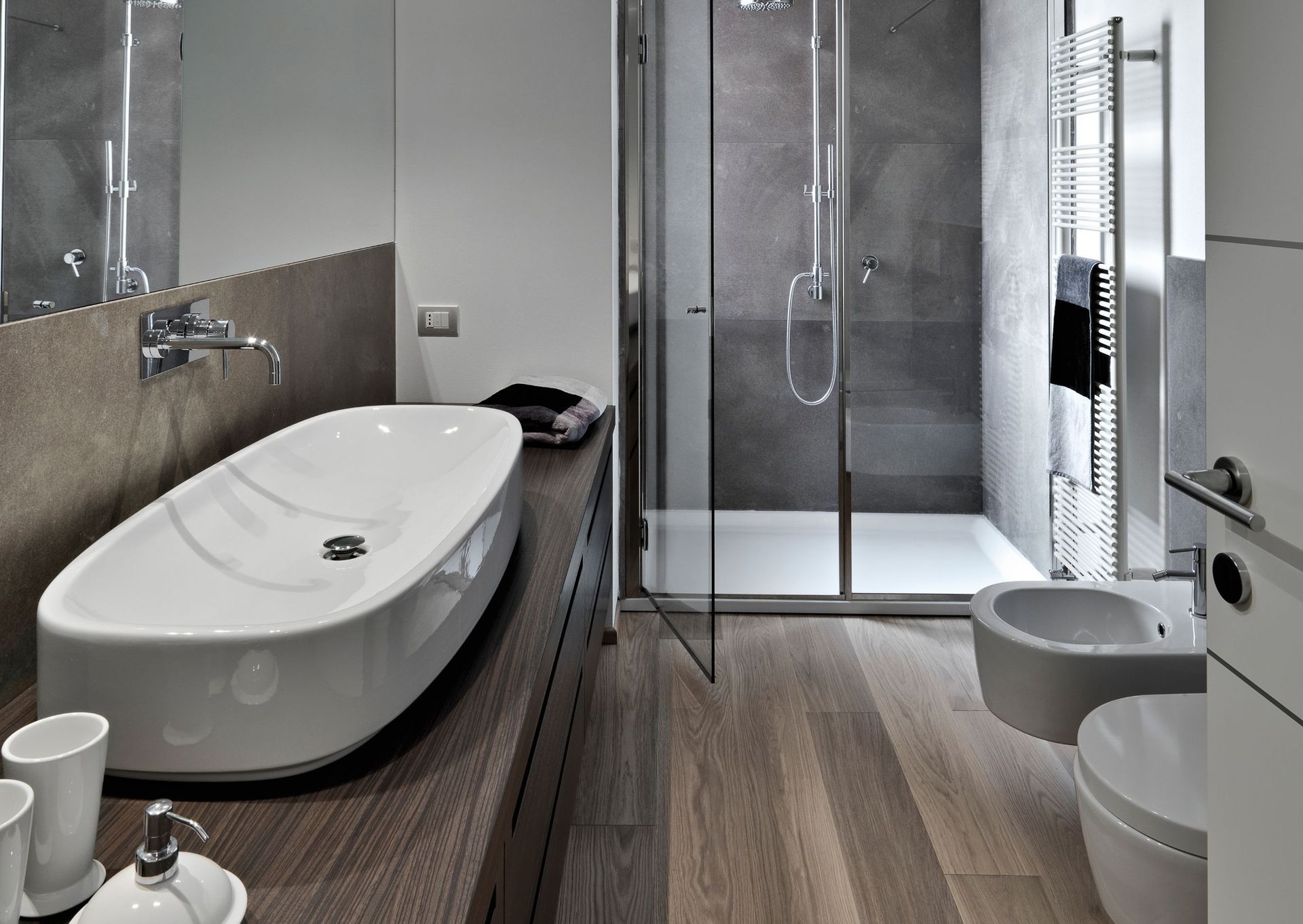 Modern bathroom with a white sink, shower, toilet, and wood-look floor. Gray walls, silver fixtures.