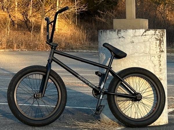 A black bmx bike is parked on a concrete post in a parking lot