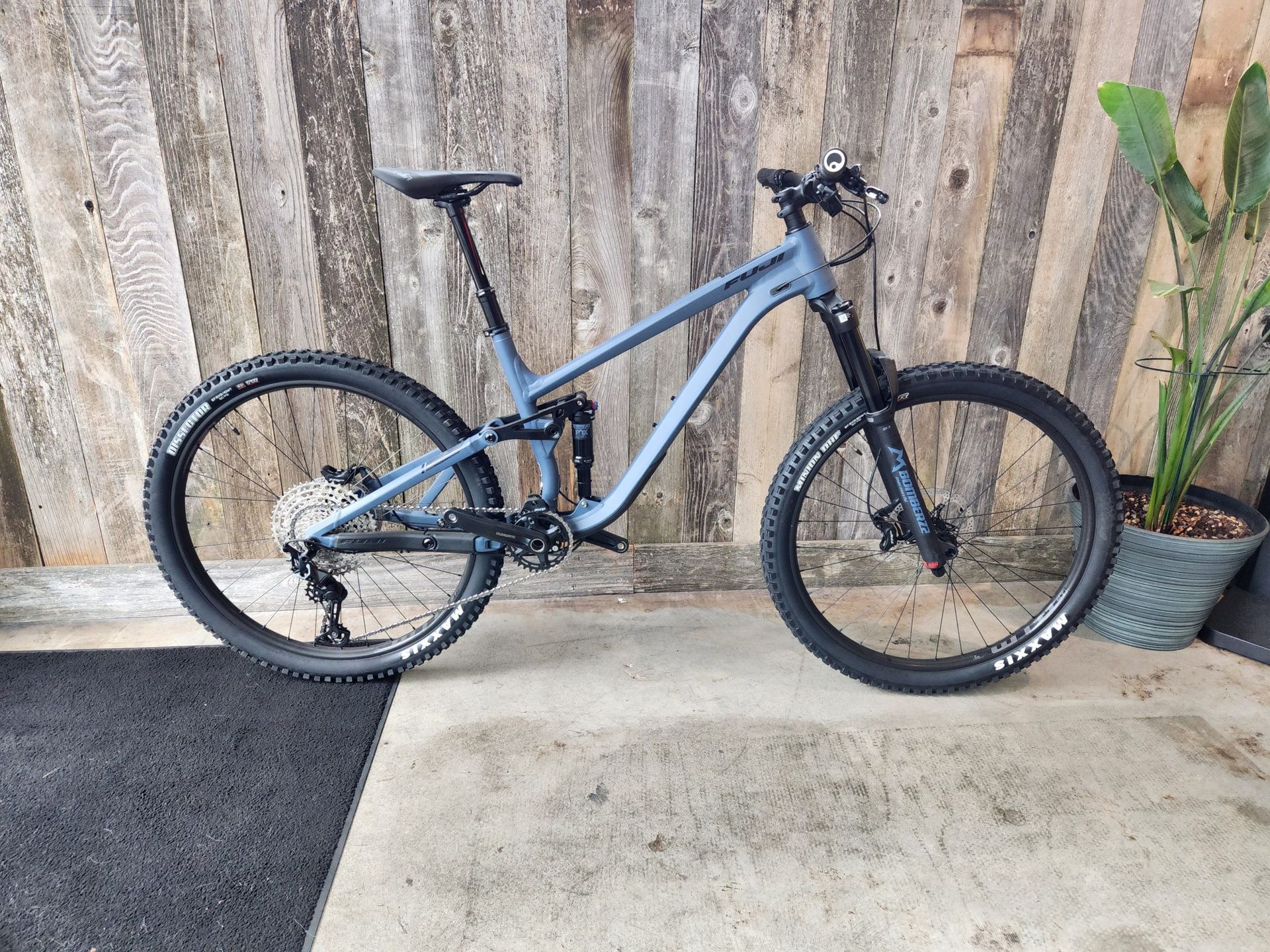 A blue mountain bike is parked in front of a wooden wall.