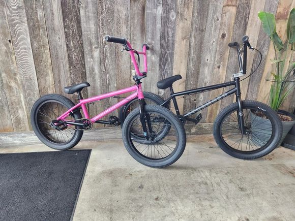 Two bmx bikes are parked next to each other in front of a wooden wall.