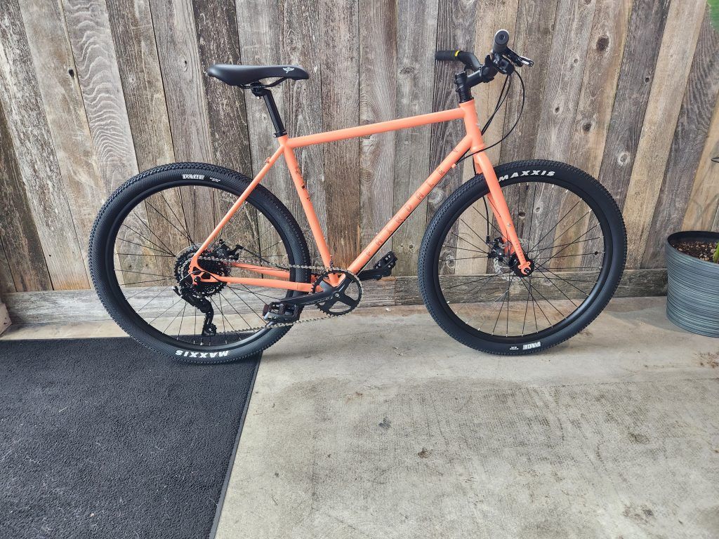 A bicycle is parked on a sidewalk in front of a wooden fence.