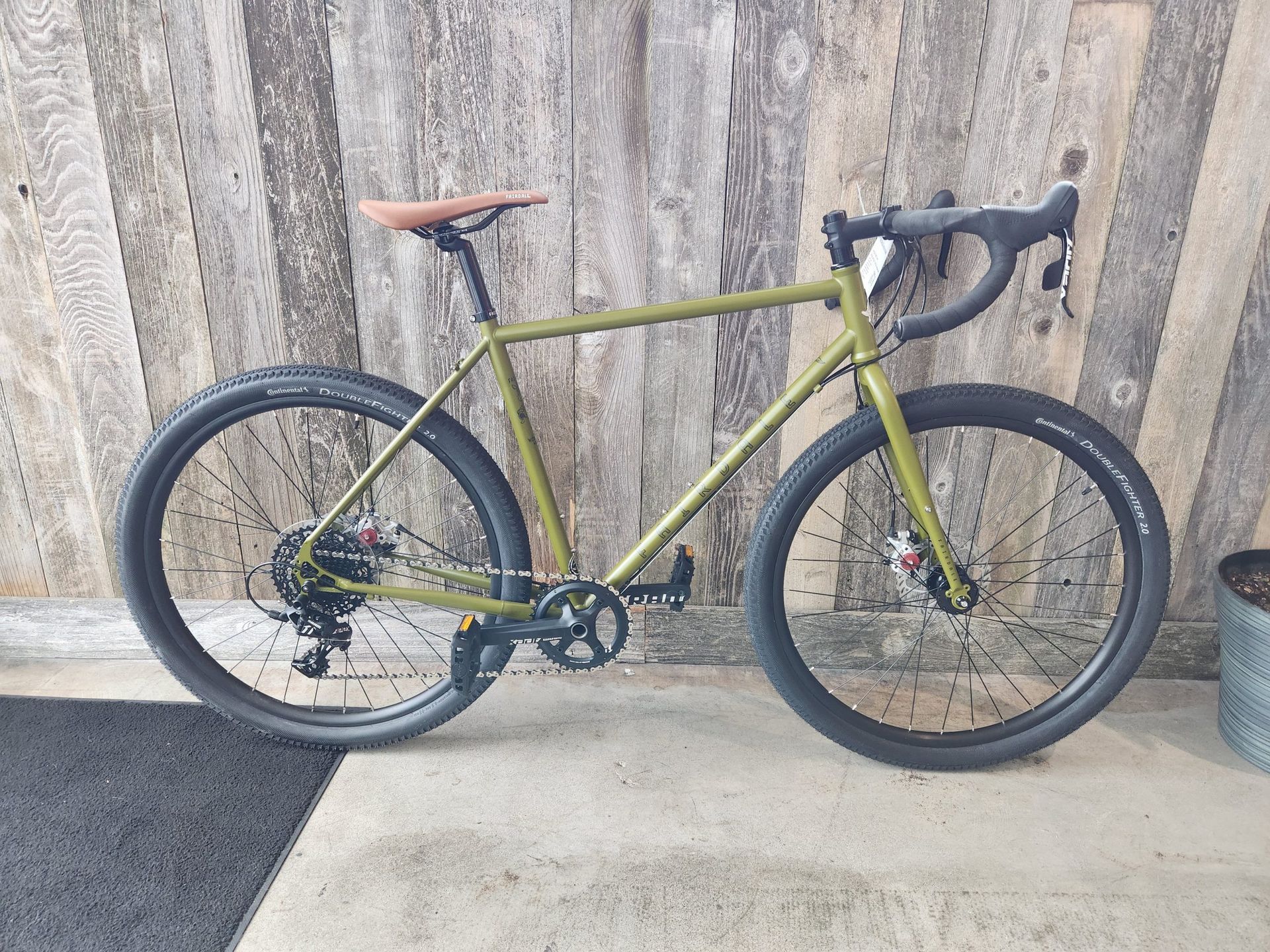 A green bicycle is parked on a sidewalk in front of a wooden wall.
