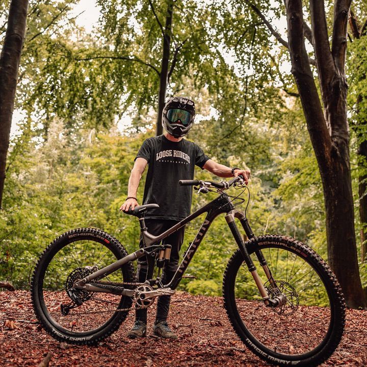 A man wearing a helmet is standing next to a mountain bike in the woods.