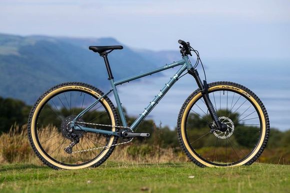 A blue mountain bike is parked on top of a grassy hill.