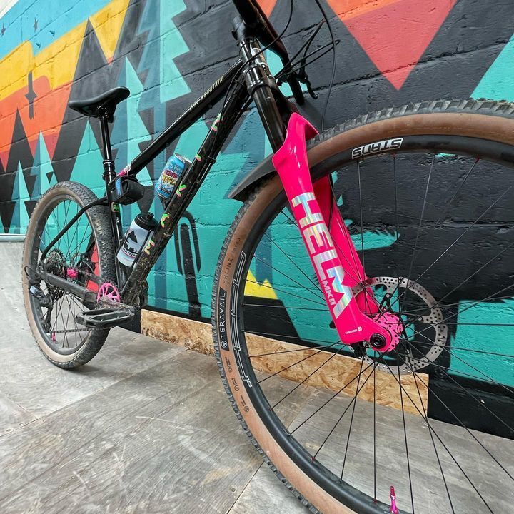 A bicycle with a pink fork is parked in front of a colorful wall.