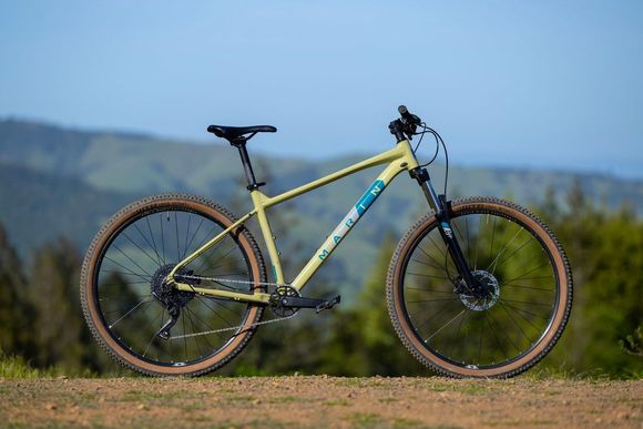 A yellow mountain bike is parked on top of a dirt hill.