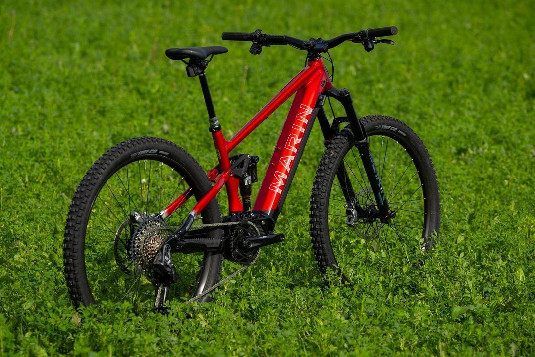 A red mountain bike is parked in a grassy field.
