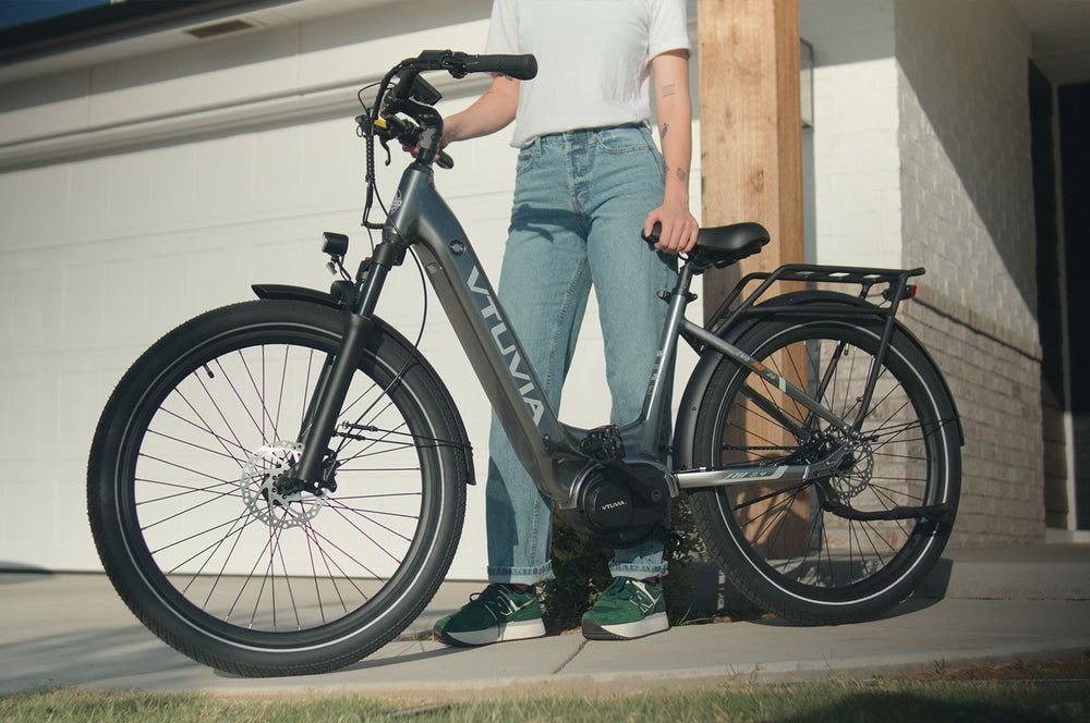 A woman is standing next to an electric bike in front of a garage door.
