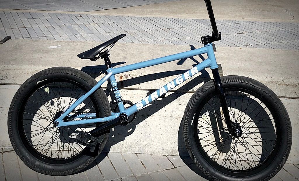 A blue bmx bike is parked on a brick sidewalk