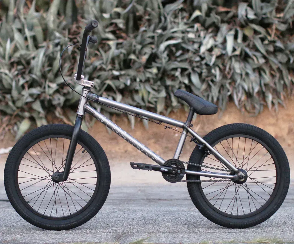 A bmx bike is parked on the side of the road in front of a bush.