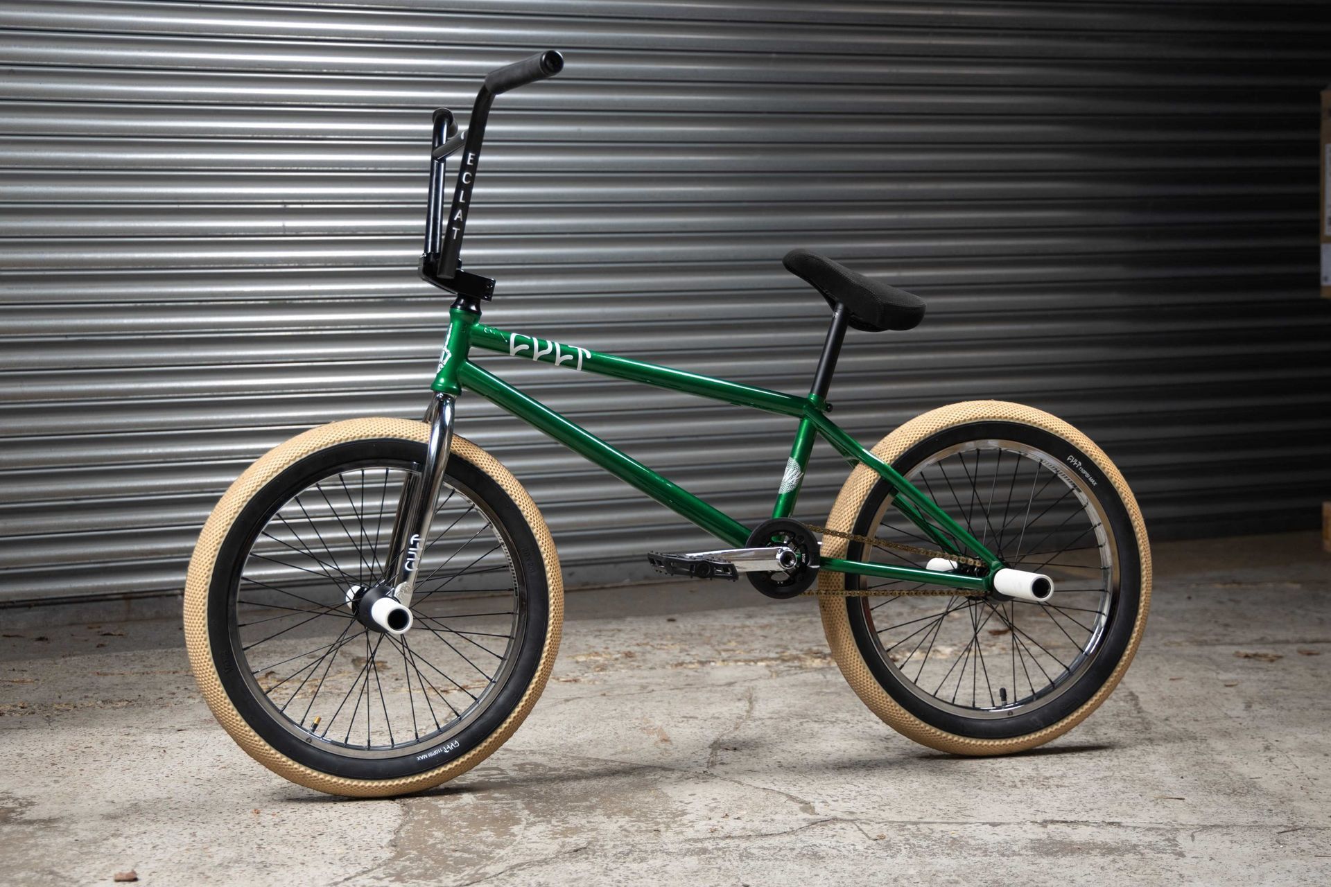 A green bmx bike is parked in front of a metal wall.
