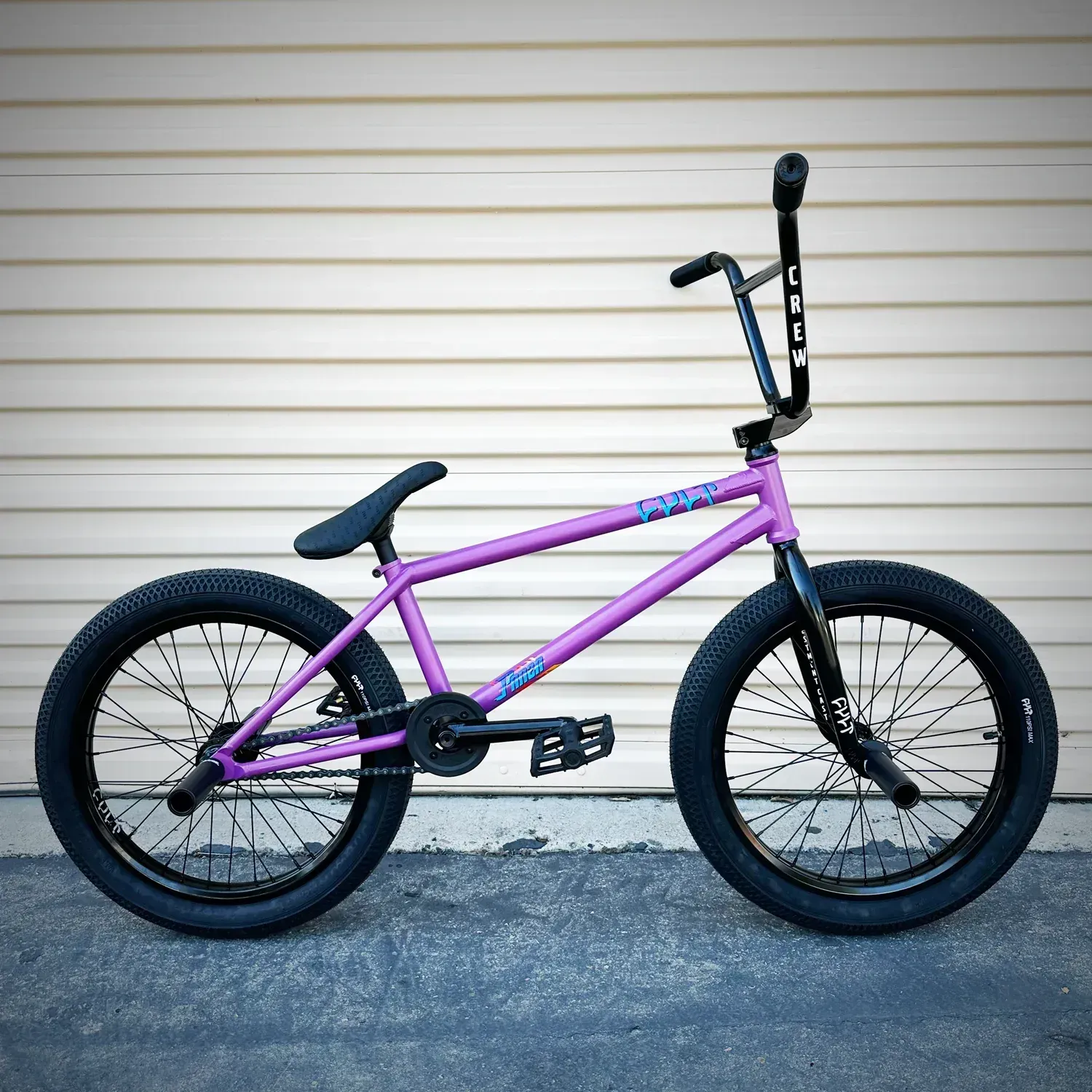A purple bmx bike is parked in front of a white wall