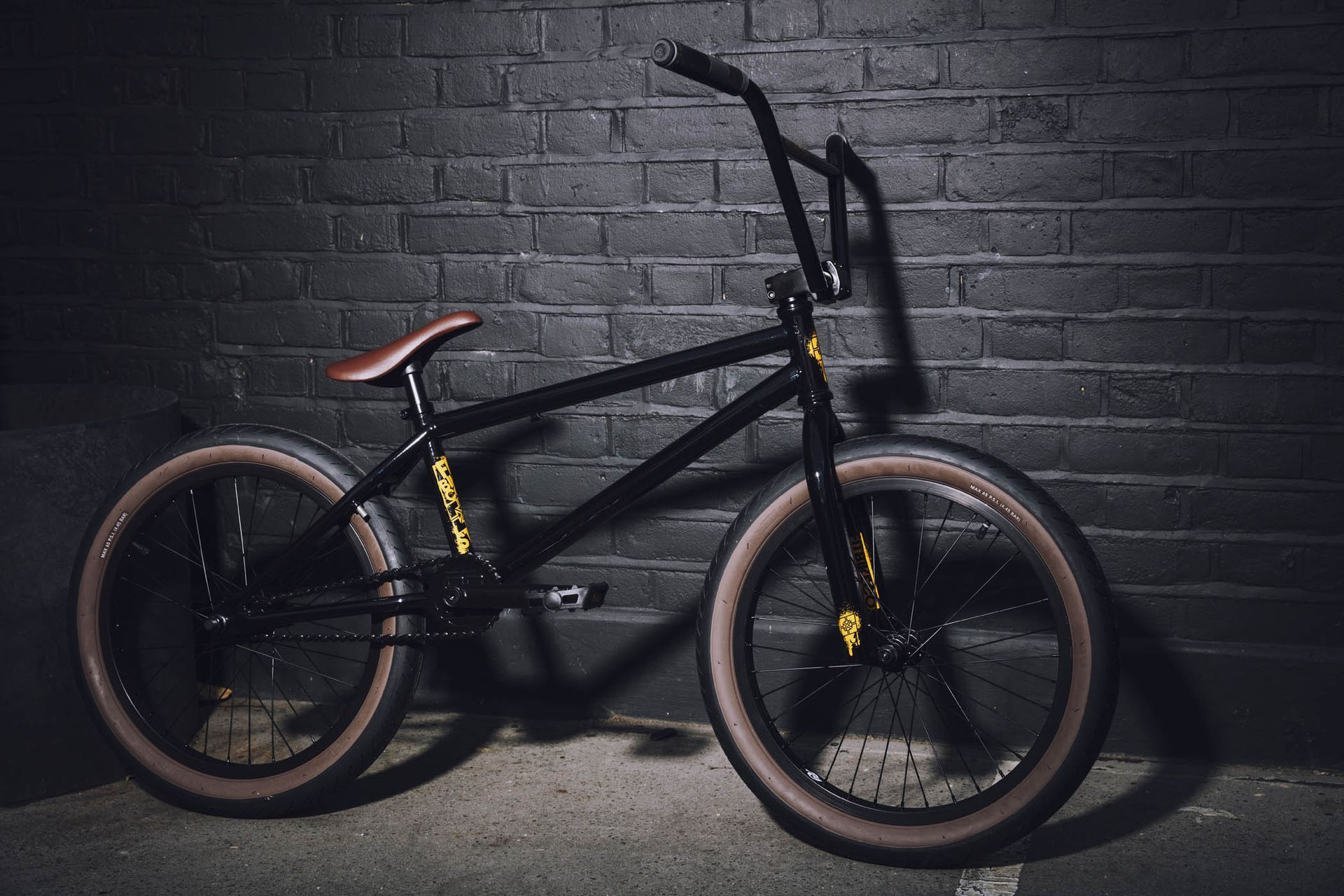 A black bmx bike is parked in front of a black brick wall.