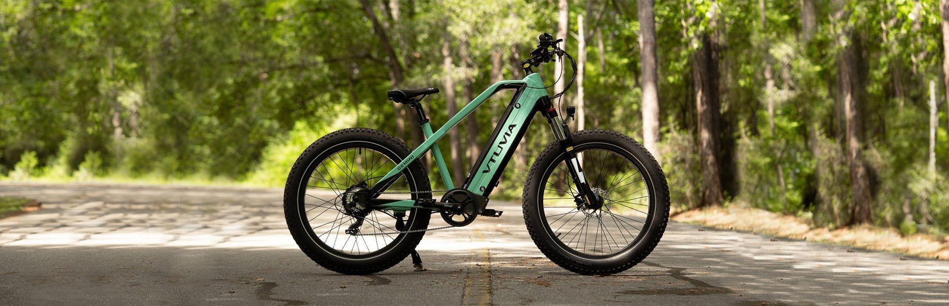 A green electric bike is parked on the side of a road in the woods.