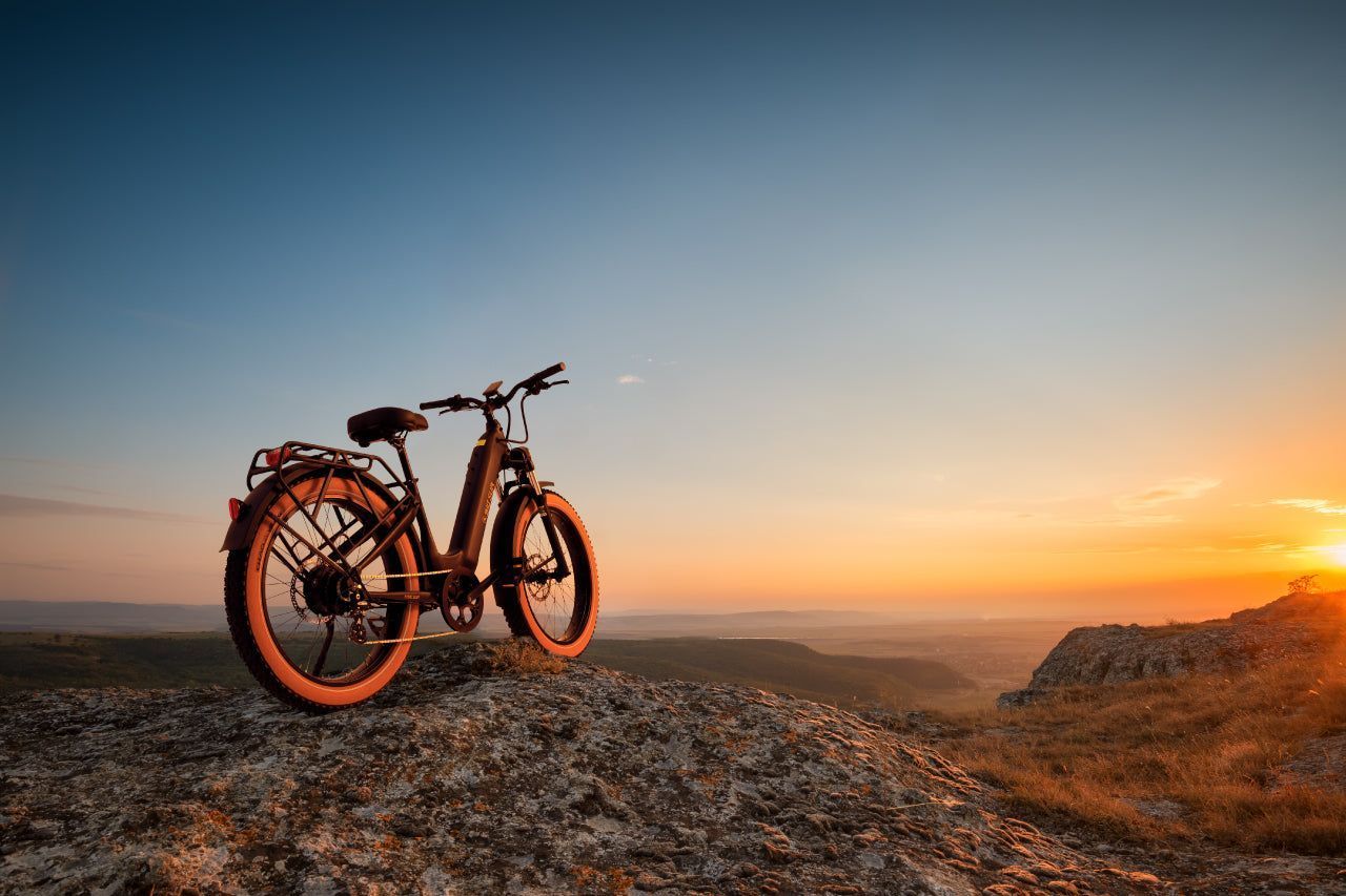 A bicycle is parked on top of a rocky hill at sunset.