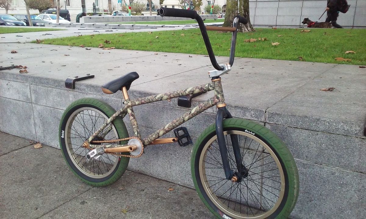 A bmx bike with green tires is parked on the sidewalk