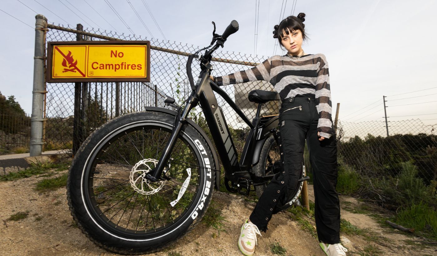 A woman is standing next to a bicycle in front of a no campfire sign.