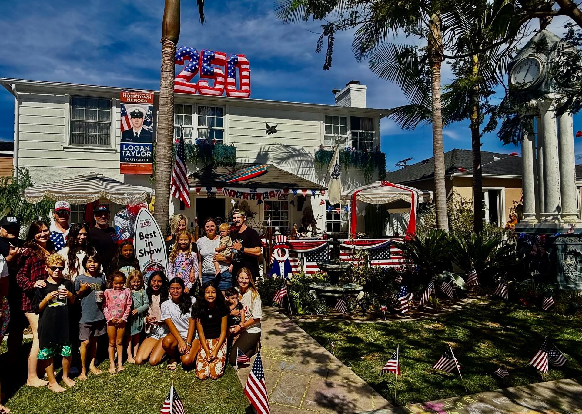 Crowd gathered outside a house for a patriotic parade, with American flags and red-white-blue decorations.