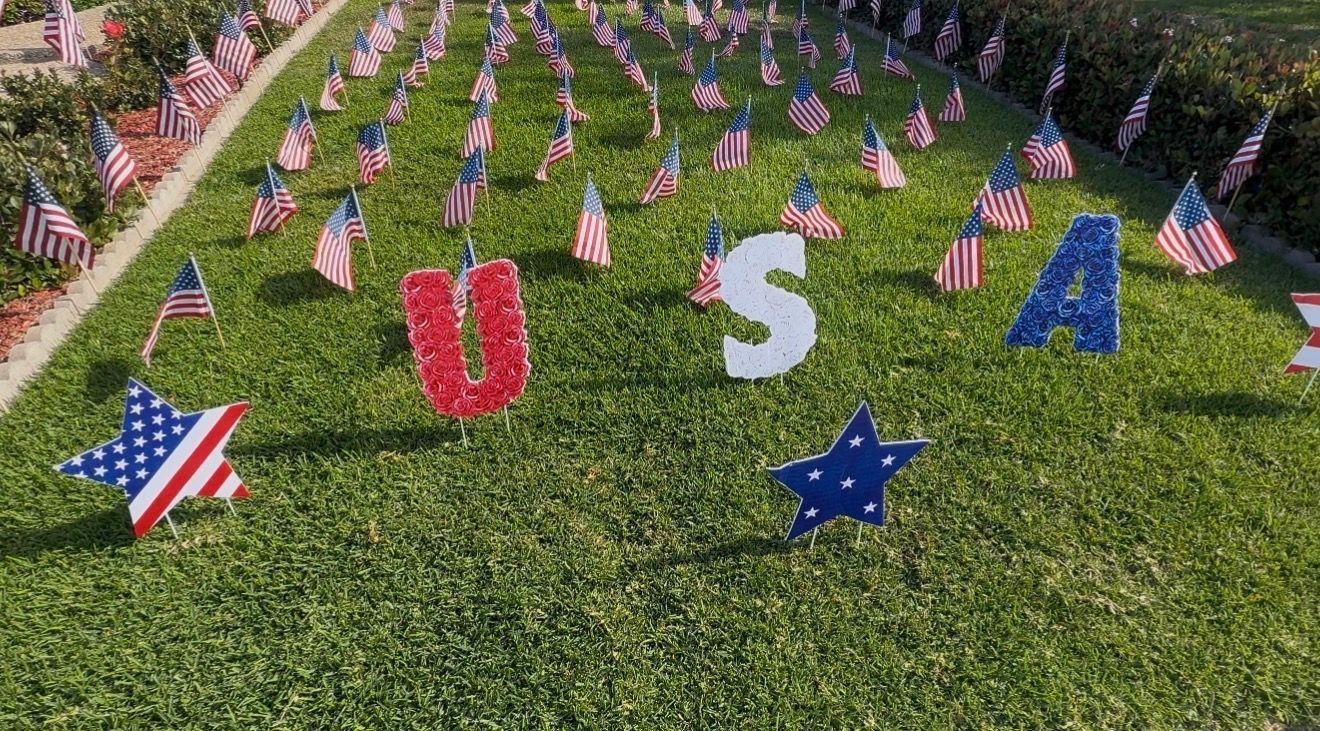 Thousands of small American flags forming “USA” on green grass with patriotic star decorations