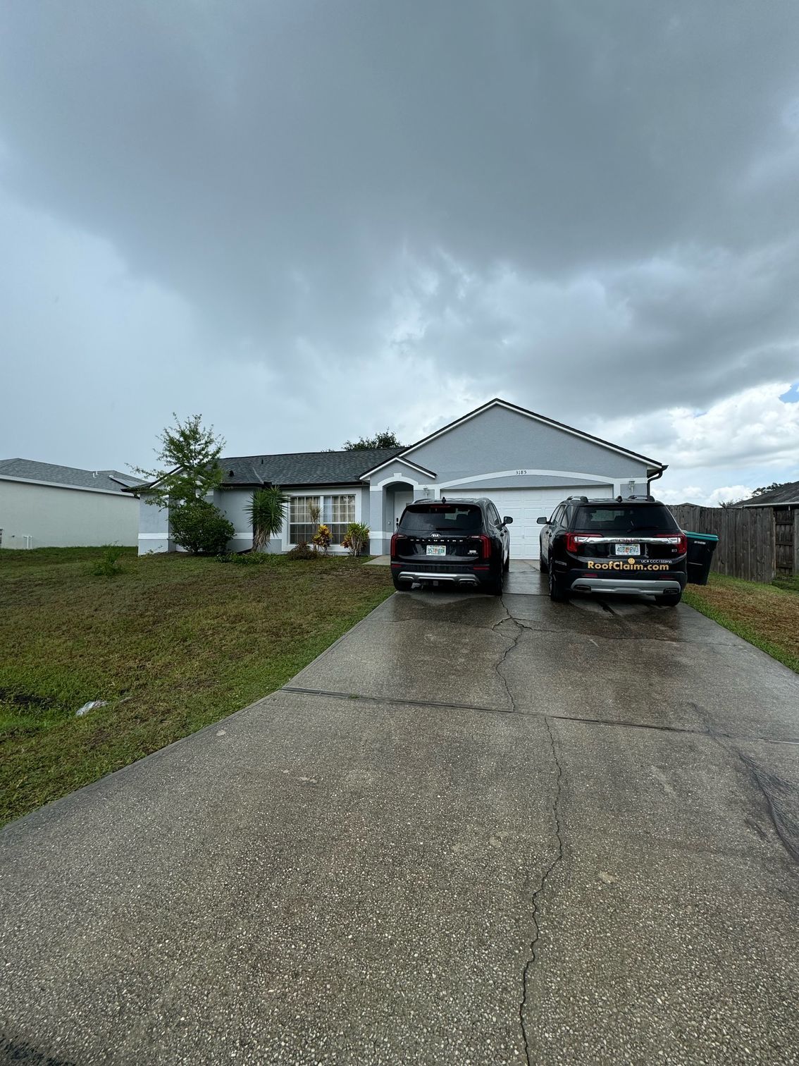 Two cars are parked in front of a house on a cloudy day.