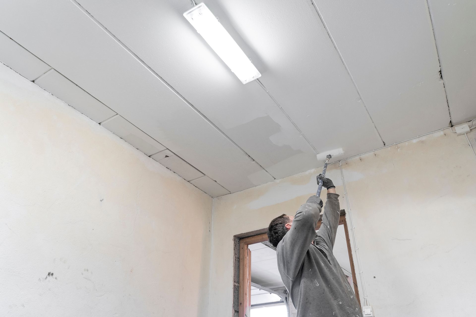A man is painting the ceiling of a room with a roller.