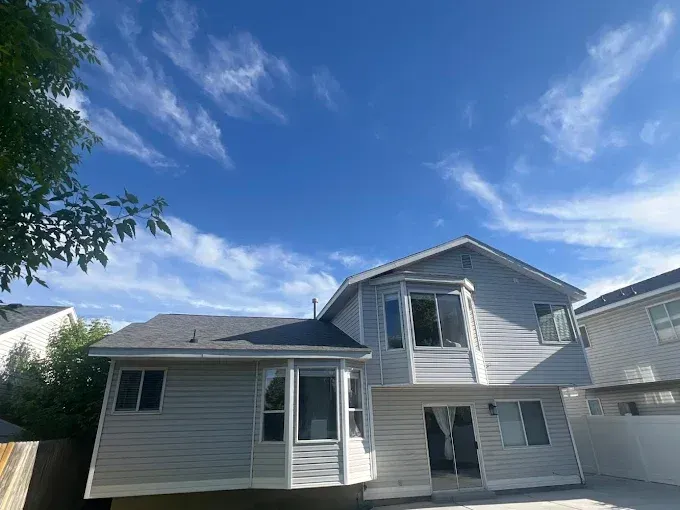 Two-story gray house with bay windows, under a blue sky with wispy clouds.
